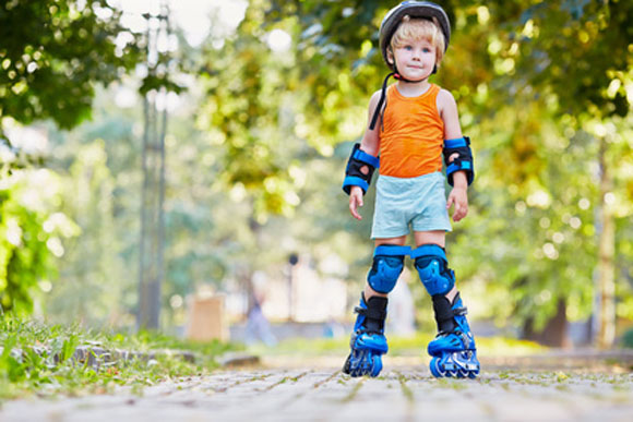 Little boy in protective equipment and rollers stands on walkway